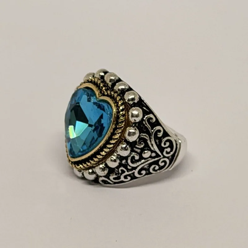 Anel prateado com cristal azul em coração, moldura dourada e arabescos nas laterais — ref. ANQ0169A
