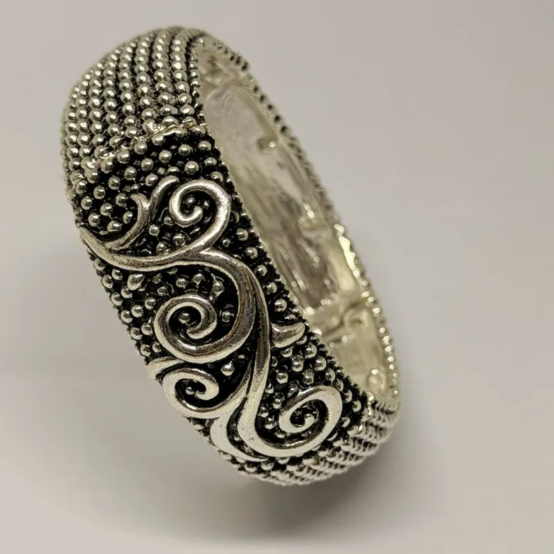 Bracelete elástico prateado com volutas esculpidas sobre textura granulada