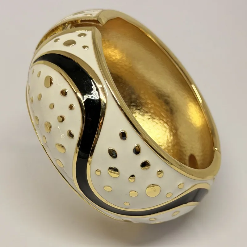 Bracelete largo dourado com esmalte branco e preto em padrão abstrato com poás dourados