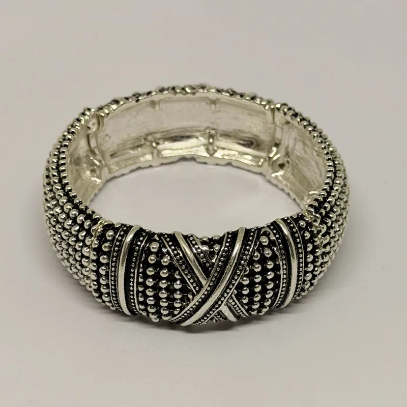 Bracelete prateado com textura de bolinhas e detalhe central em X trançado