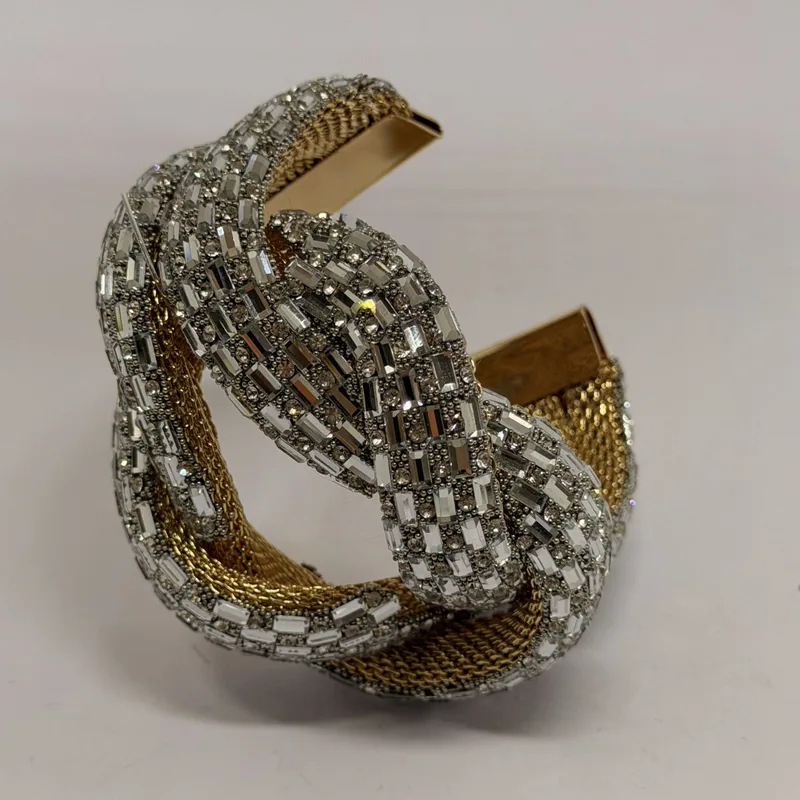 Cuff em formato de nó com cristais baguete sobre malha dourada